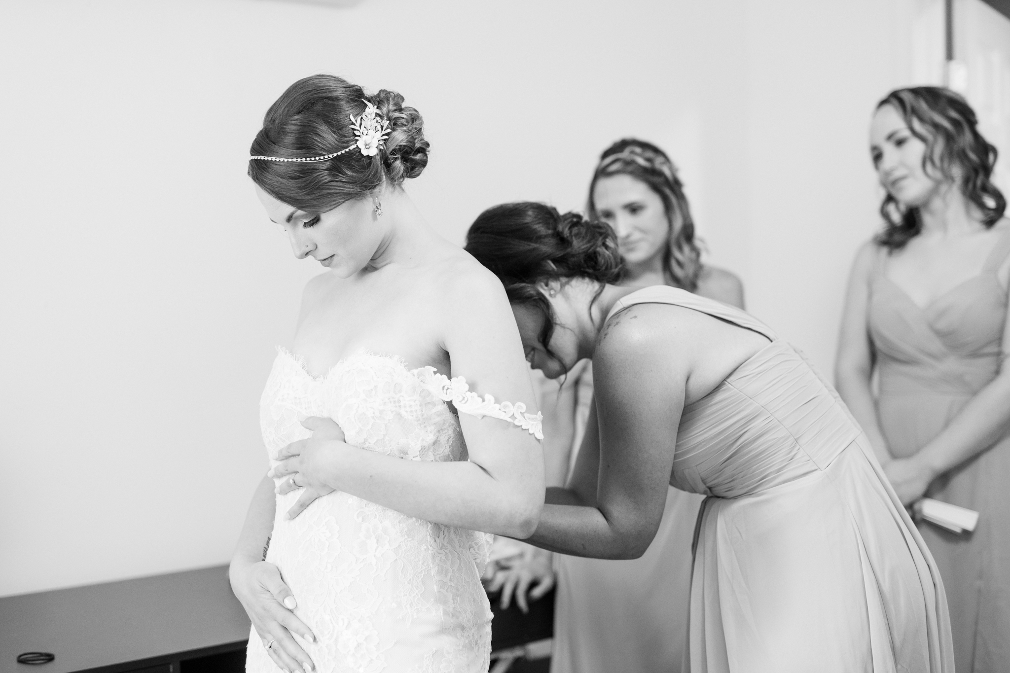 Maryland bride getting ready on her wedding day with her bridesmaids. Her bridesmaid is helping to tie her corset dress