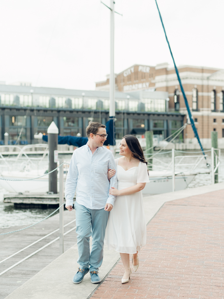 Engaged couple walking along water in Fells Point for their Baltimore engagement session. 