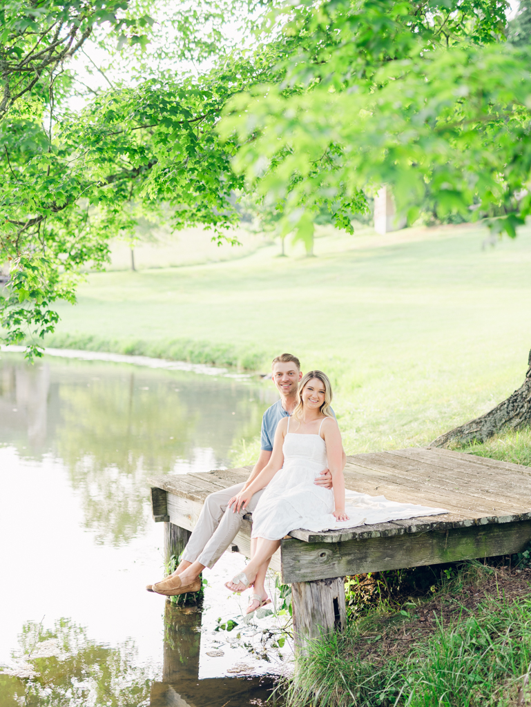 Victoria & Jacob sitting on the dock of the pond during golden hour for their engagement session at Cold Saturday Farm