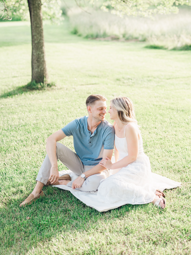 Victoria & Jacob laughing together on a blanket during golden hour for their engagement session at Cold Saturday Farm