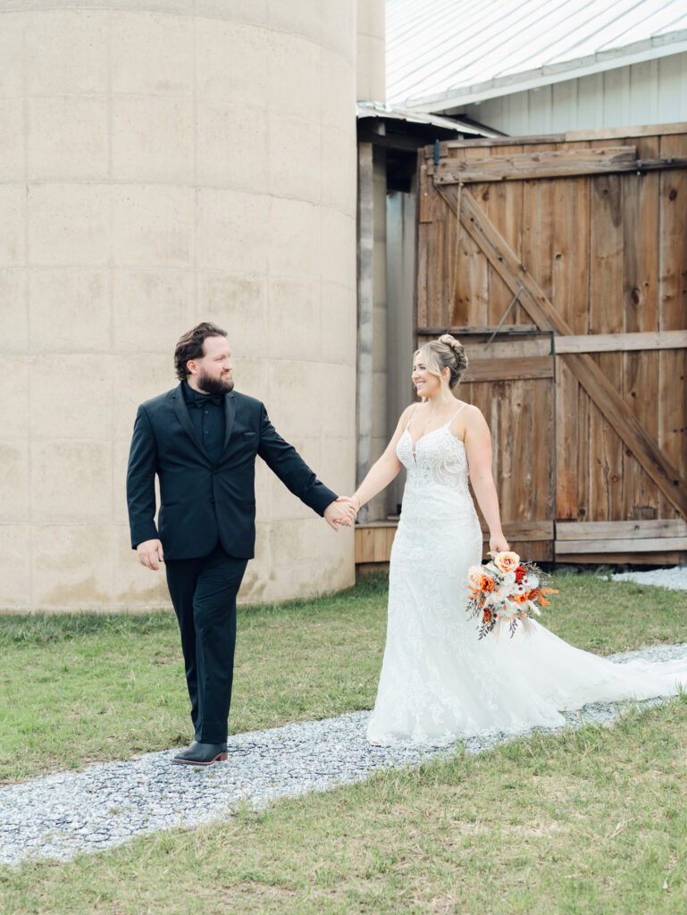 Bride and groom holding hands and walking outside the barn at The Hummingbird Chateau on their wedding day