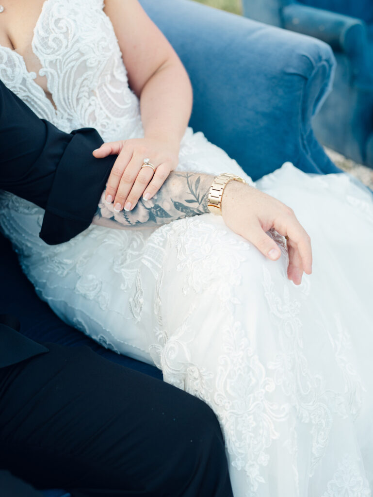 bride's hand with wedding band and engagement ring resting on groom's tattooed arm